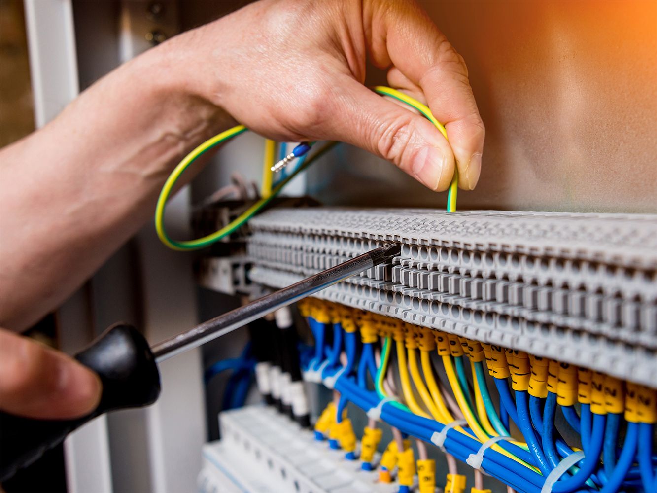 Eine Person arbeitet an einem Panel mit Kabeln und führt technische Anpassungen durch.